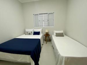 two beds in a white room with a window at Casa bem Equipada 3 quartos in Marília