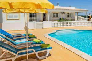 a house with a swimming pool with chairs and an umbrella at Casa Luz in Lagoa