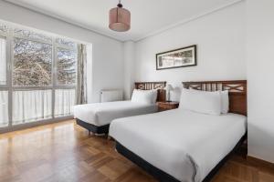 two beds in a room with two windows at Apartamentos El Cid in Burgos