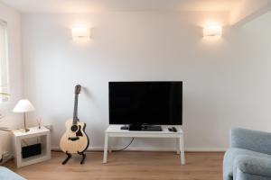 ein Wohnzimmer mit einem TV und einer Gitarre an der Wand in der Unterkunft Olivera House in Redruth