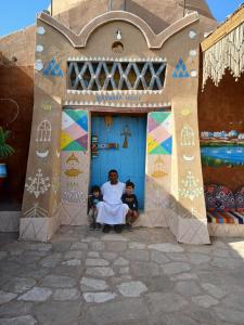 um homem e duas crianças sentados à frente de uma porta azul em Kabara Nubian House em Abu Simbel