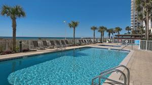 a large swimming pool with chairs and palm trees at PARKING INCLUDED-Beachfront 2BD Ocean Villa! Gorgeous Amenities, Private Complex in Panama City Beach
