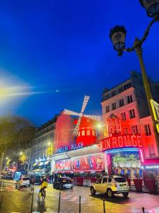 a city street with cars and buildings with neon lights at Appartement Cosy Paris Montmartre in Paris