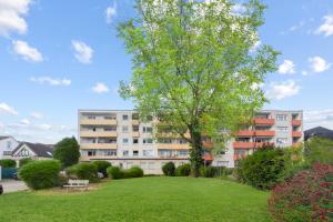 an apartment building with a tree in a park at VINFUL: Premium-Apartment mit Balkon und Parkplatz in Mülheim an der Ruhr