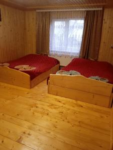 two beds in a room with wooden floors and a window at Смерека in Mykulychyn