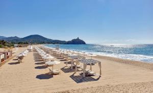 una fila de sillas y sombrillas en una playa en Baia Di Chia Resort Sardinia, Curio Collection By Hilton, en Chia