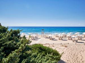 a beach with chairs and umbrellas and the ocean at Baia Di Chia Resort Sardinia, Curio Collection By Hilton in Chia