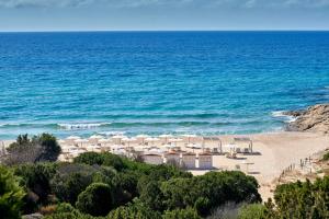 a beach with white umbrellas and the ocean at Baia Di Chia Resort Sardinia, Curio Collection By Hilton in Chia