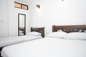 Duas camas num quarto branco com um espelho. em Hotel La Casa Del Viajero em Cartagena das Índias