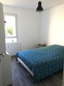 Schlafzimmer mit einem Bett mit blauer Bettdecke und einem Fenster in der Unterkunft Les jardins du Moiron in Le Champ-près-Froges