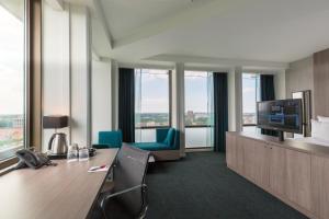 una oficina con escritorio, TV y ventanas en Leonardo Hotel Amsterdam Rembrandtpark en Ámsterdam