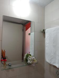 La salle de bains est pourvue d'un miroir, d'une serviette et de fleurs. dans l'établissement Hospedagem Virginia Bracelli, à Campos do Jordão