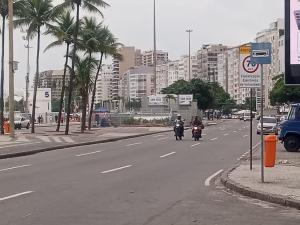 two people riding motorcycles down a city street with palm trees at Copacabana AP na esquina da praia in Rio de Janeiro