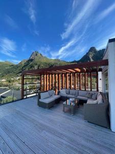 eine Holzterrasse mit Sofas, Tischen und Bergen in der Unterkunft Leilighet med sjøutsikt og privat takterrasse. Parkering in Svolvær