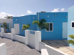 a blue house with a white fence and palm trees at Apricity Suites Aruba in Noord
