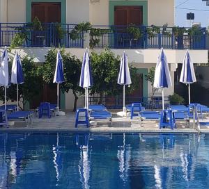 a swimming pool with blue chairs and umbrellas at George Studios Stalida in Stalís