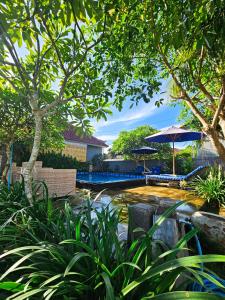 a swimming pool with an umbrella and trees and bushes at Hokita Home Stay in Nusa Lembongan