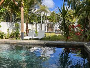 a pool with two white chairs and palm trees at Tropical 3-bedrooms Coastal Residence Creolia2 in Pointe aux Cannoniers