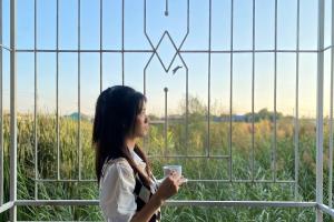 a woman standing in front of a fence holding a coffee cup at Grand Sansook Omnoi in Ban Khlong Om Noi