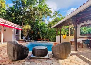 a swimming pool with wicker chairs next to a house at Villa Mahogany confort, spacieuse in Le François