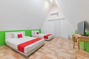 two beds in a room with a television and a desk at RedDoorz Syariah Plus Near Sukabumi Station in Sukabumi