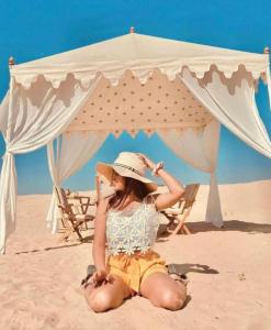 Sam dunes desert safari camp في جيلسامر: امرأة جالسة على الشاطئ تحت خيمة