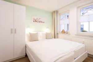 a white bedroom with a white bed and two windows at Fewo Auszeit im Haus Strandburg in Binz