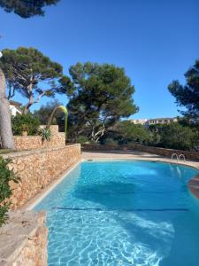 ein blauer Pool mit einer Steinmauer und Bäumen in der Unterkunft Appartement Ferrera Park 408 vue mer in Cala Ferrera