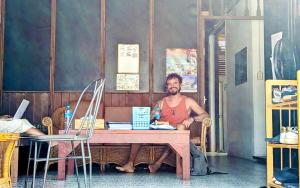 mężczyzna siedzący przy stole w pokoju w obiekcie Aforetime House @ Samui w mieście Taling Ngam Beach