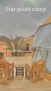 a person sitting in chairs on a deck with a tent at Star Guide Camp in Wadi Rum