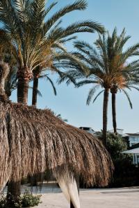 two palm trees with a straw roof on a beach at Prinsotel La Dorada & Spa in Playa de Muro