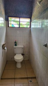 a small bathroom with a toilet and a window at Tradewins Cottage in Diani Beach