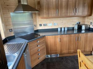 a kitchen with wooden cabinets and a stove at Hazel Lodge luxury log cabin in South Wingfield