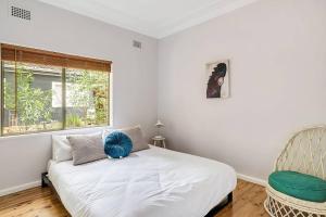 a bedroom with a bed and a chair and a window at Pearl Beach House - 2 min to sand & sea - 2 semis in Pearl Beach