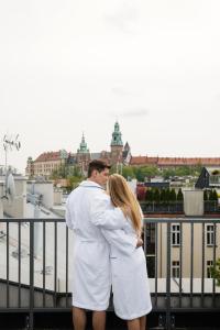 un homme et une femme vêtus de blanc debout sur un balcon dans l'établissement Golden Queen Deluxe Jacuzzi Apartments - Old Town, à Cracovie