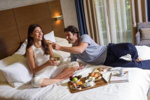 Um homem e uma mulher sentados numa cama a comer. em Anatolia Hotel em Tessalônica