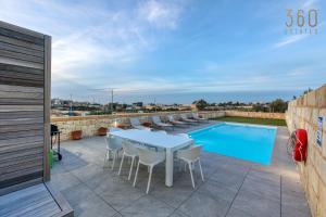 een patio met een tafel en stoelen naast een zwembad bij LUX Villa with Private Pool, BBQ & Rooftop Oasis by 360 Estates in Kalkara