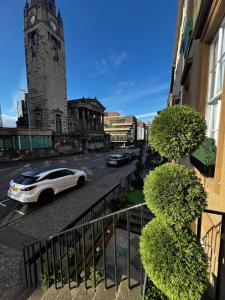 a white car driving down a street with a clock tower at Amani Apartments - Glasgow City Centre in Glasgow