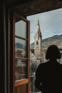 une personne qui regarde par une fenêtre une église dans l'établissement Arthotel Lasserhaus, à Brixen