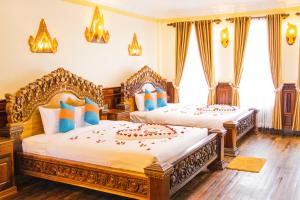 two beds in a bedroom with wooden floors and windows at Puok Hotel in Phumĭ Puŏk Chăs