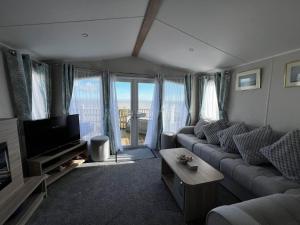 a living room with a couch and a tv at 6 Berth Caravan With Stunning Sea Views And Decking To Relax On, Ref 32048az in Lowestoft