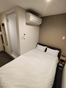 1 dormitorio con 1 cama blanca y aire acondicionado en FLYCAT INN 伊勢, en Ise