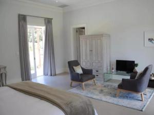 a bedroom with a bed and two chairs and a television at Chambray Estate - The Terraces in the Vines in Franschhoek