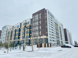 a large building in a parking lot in the snow at Apartaments COSTA ЖК Алпамыс in Astana