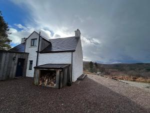 een klein wit huis met een stapel brandhout bij Alt-Na-Slat Cottage in Invergarry