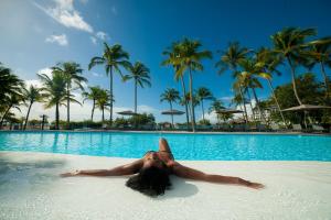 Una donna stesa in acqua in una piscina di Mahogany Hotel Residence & Spa a Le Gosier