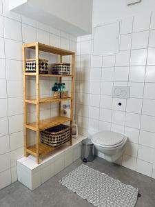 a white tiled bathroom with a toilet and a shelf at Urban Living unter den Dächern der Göttinger Altstadt in Göttingen