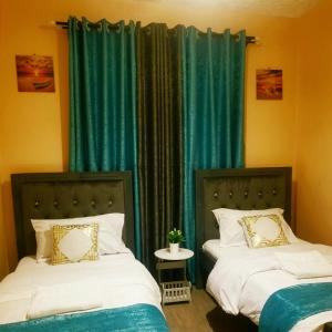 two beds in a room with green curtains at T-Tree Paradise Apartments in Embu