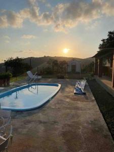 een zwembad met stoelen en de zonsondergang op de achtergrond bij Casa perfeita pra fim de semana e feriadões in Vitória de Santo Antão