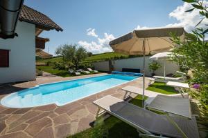 uma piscina com duas cadeiras e um guarda-sol em Ferienwohnungen Lanserhof em Appiano sulla Strada del Vino